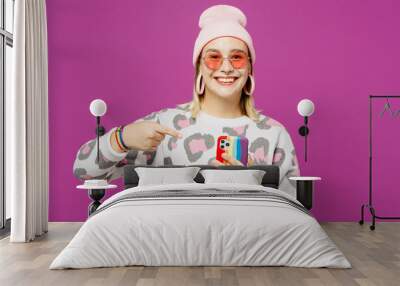 Young happy lesbian woman wear pink animal clothes hold in hand use point index finger on mobile cell phone isolated on plain purple background studio portrait Pride day June month love LGBTQ concept Wall mural