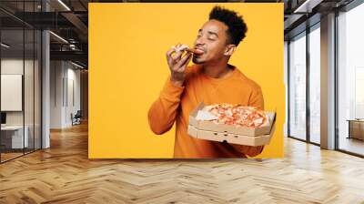 Young happy man he wears orange sweatshirt casual clothes holding italian pizza in cardboard flatbox isolated on plain yellow background. Proper nutrition healthy fast food unhealthy choice concept. Wall mural