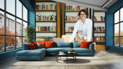 Young happy successful employee IT business woman she wearing glasses white shirt casual clothes use laptop pc computer stand near table work at office desk with pc laptop. Achievement career concept. Wall mural