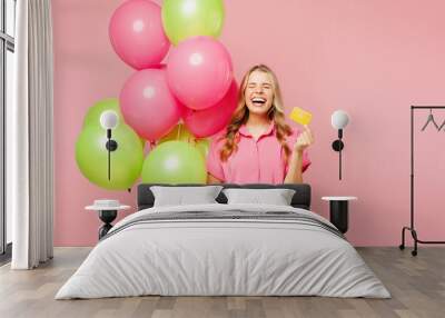 Young happy thankful excited woman wearing shirt celebrating birthday holiday and hold bunch of colorful air balloons,mock up of credit bank card isolated on plain pink background. Lifestyle concept Wall mural