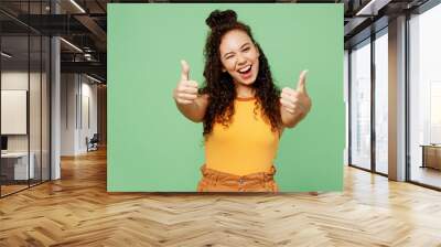 Young happy woman of African American ethnicity wear yellow tank shirt top showing thumb up like gesture blink eye isolated on plain pastel light green background studio portrait. Lifestyle concept. Wall mural