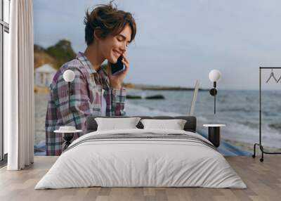 Young IT woman wear shirt casual clothes work hold use laptop pc computer speak on mobile cell phone sits rest on sea ocean sand shore beach outdoor seaside in summer day free time. Lifestyle concept. Wall mural