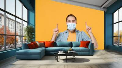 Young man in sterile face mask posing isolated on yellow background studio portrait. Epidemic pandemic rapidly spreading coronavirus 2019-ncov sars covid-19 flu virus concept. Point index fingers up. Wall mural