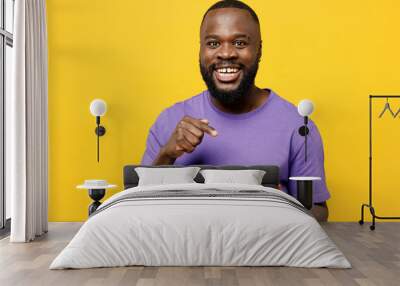 Young man of African American ethnicity he wears casual clothes purple t-shirt hold in hand use point index finger on mobile cell phone isolated on plain yellow background studio. Lifestyle concept. Wall mural