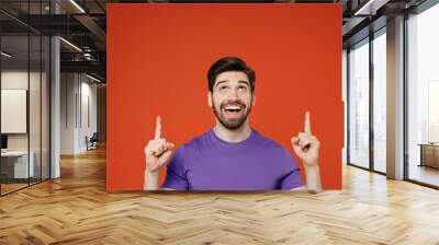 Young man wear casual basic purple t-shirt pointing index finger overhead on indicate on workspace area copy space mock up isolated on plain orange background studio portrait People lifestyle concept Wall mural