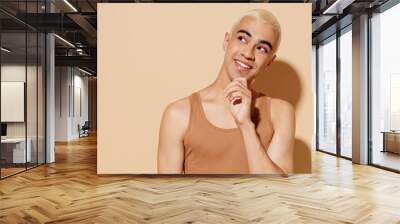 Young minded fun blond latin american gay man 20s with make up in beige tank shirt looking aside prop up chin isolated on plain light ocher background studio portrait People lgbt lifestyle concept Wall mural