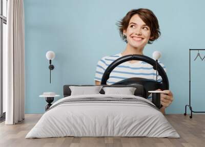 Young minded happy woman wears striped t-shirt casual clothes hold steering wheel driving car look aside on area isolated on plain pastel light blue cyan background studio portrait. Lifestyle concept. Wall mural