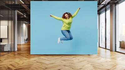 Young overjoyed excited chubby overweight plus size big fat fit woman wear green sweater jump high with outstretched hands isolated on plain blue background studio portrait. People lifestyle concept. Wall mural