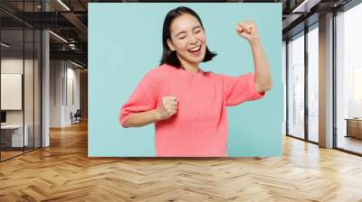 Young overjoyed happy excited woman of Asian ethnicity 20s wear pink sweater do winner gesture celebrate clenching fists say yes isolated on pastel plain light blue color background studio portrait Wall mural