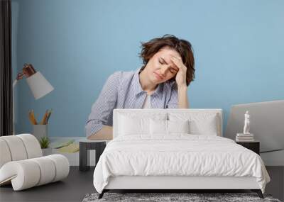 Young sad frustrated tired disappointed employee business woman in casual shirt sit work at white office desk with pc laptop prop up forehead have headache isolated on pastel blue background studio. Wall mural