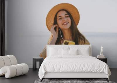 Young satisfied woman in straw hat shirt summer casual clothes earphones use mobile cell phone listen music outdoors at sunrise sun dawn over sea background People vacation lifestyle journey concept Wall mural