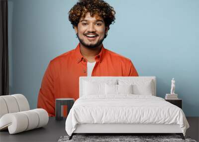 Young smiling cheerful fun cool Indian man wear orange red shirt white t-shirt looking camera with toothy smile isolated on plain pastel light blue cyan background studio portrait. Lifestyle concept. Wall mural