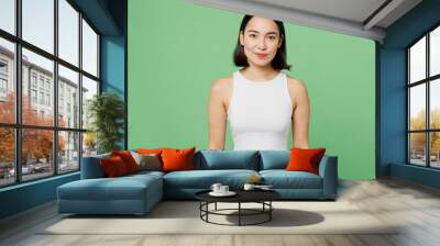 Young smiling cheerful fun happy cool beautiful woman of Asian ethnicity wear white tank shirt looking camera isolated on plain pastel light green background studio portrait. People lifestyle concept. Wall mural