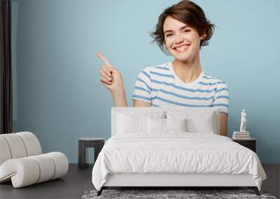 Young smiling cheerful fun woman wears striped t-shirt casual clothes point index finger aside on area mock up isolated on plain pastel light blue cyan background studio portrait. Lifestyle concept. Wall mural