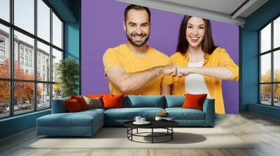 Young smiling cheerful happy couple two friends family man woman together in yellow casual clothes looking camera giving a fist bump in agreement isolated on plain violet background studio portrait. Wall mural