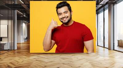 Young smiling cheerful happy Indian man he wearing red t-shirt casual clothes doing phone gesture like says call me back isolated on plain yellow orange background studio portrait. Lifestyle concept. Wall mural