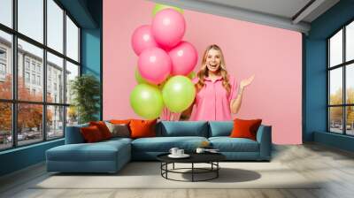 Young smiling cheerful woman wear shirt celebrating birthday holiday and hold bunch of colorful air balloons spread hands look camera isolated on plain pastel light pink background. Lifestyle concept. Wall mural