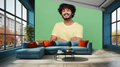 Young smiling confident happy Indian man 20s in basic yellow t-shirt hold hands crossed folded look camera isolated on plain pastel light green background studio portrait. People lifestyle concept Wall mural