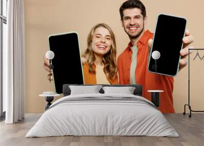 Young smiling couple two friend family man woman wear casual clothes hold in hand use showing close up mobile cell phone with blank screen workspace area together isolated on plain beige background. Wall mural