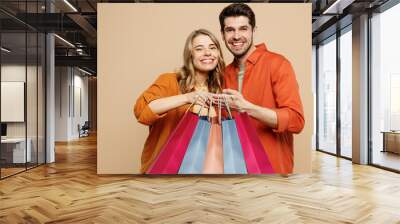 Young smiling fun couple two friends family man woman wears casual clothes hold shopping paper package bags look camera together isolated on plain beige background. Black Friday sale buy day concept. Wall mural