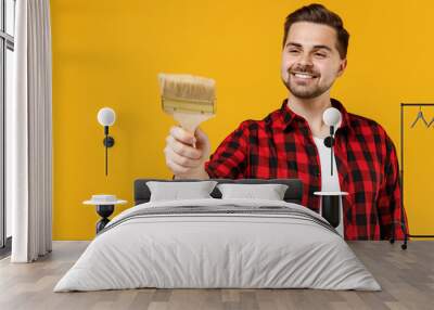 Young smiling fun employee handyman man in checkered shirt using paint brush working isolated on yellow background studio. Instruments accessories for renovation apartment room. Repair home concept. Wall mural