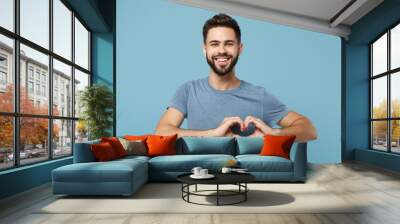 Young smiling handsome man in casual clothes posing isolated on blue wall background, studio portrait. People lifestyle concept. Mock up copy space. Showing shape heart with hands, heart-shape sign. Wall mural