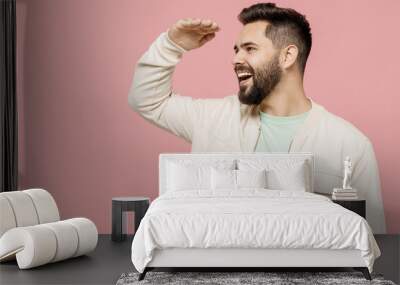 Young smiling happy caucasian man 20s wearing trendy jacket shirt hold hand at forehead look far away distance isolated on plain pastel light pink background studio portrait. People lifestyle concept. Wall mural