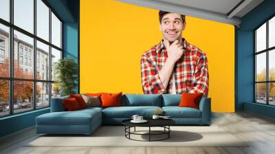 Young smiling happy Caucasian man he wears red checkered shirt casual clothes put hand prop up on chin, lost in thought and conjectures isolated on plain yellow orange background. Lifestyle concept. Wall mural