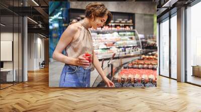 Young smiling happy caucasian woman in casual clothes shopping at supermaket greengrocery store buy choose red strawberry berries fruit inside hypermarket. People lifestyle purchasing food concept. Wall mural