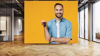 Young smiling happy cool caucasian man 20s wearing blue shirt white t-shirt hold car key fob keyless system look camera isolated on plain yellow background studio portrait. People lifestyle concept. Wall mural