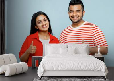 Young smiling happy couple two friends family Indian man woman wearing red casual clothes t-shirts show thumb up gesture look camera together isolated on pastel plain light blue cyan color background. Wall mural