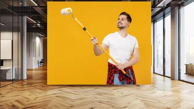 Young smiling happy employee handyman man wear t-shirt using long paint roller working isolated on yellow background studio. Instruments accessories for renovation apartment room. Repair home concept. Wall mural