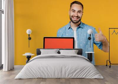 Young smiling happy freelancer copywriter man 20s wear blue shirt hold use work on laptop pc computer with blank screen workspace area sow thumb up isolated on plain yellow background studio portrait Wall mural