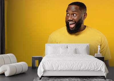 Young smiling happy fun black man 20s wearing bright casual t-shirt look aside on copy space workspace area mock up isolated on plain yellow color background studio portrait. People lifestyle concept. Wall mural