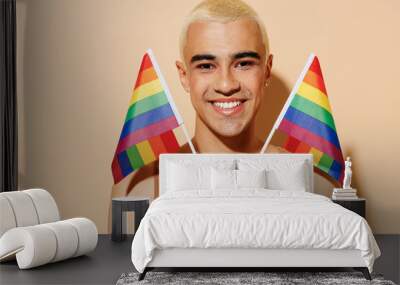 Young smiling happy fun cheerful blond latin gay man with make up in beige tank shirt holding rainbow flag isolated on plain light ocher color background studio portrait People lgbt lifestyle concept. Wall mural