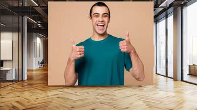 Young smiling happy fun cheerful middle eastern man wear blue t-shirt casual clothes showing thumb up like gesture isolated on plain pastel light beige background studio portrait. Lifestyle concept. Wall mural