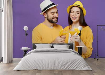 Young smiling happy fun couple two friends family man woman together in summer yellow casual clothes hat hold exotic cocktail martini raise toast isolated on plain violet background studio portrait. Wall mural