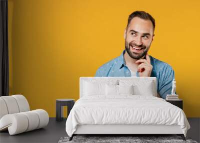 Young smiling happy pensive minded thoughtful caucasian man 20s in blue shirt white t-shirt look aside on copy space workspace area prop up chin isolated on plain yellow background studio portrait Wall mural