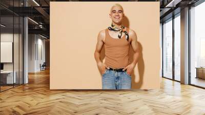 Young smiling happy trendy cool fashionable stylish blond latin gay man in beige tank shirt neck scarf isolated on plain light ocher color background studio portrait People lgbt lifestyle concept. Wall mural