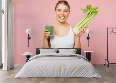 Young smiling happy woman wear white top casual clothes hold glass of celery root smoothie isolated on plain pastel light pink background. Proper nutrition healthy fast food unhealthy choice concept Wall mural