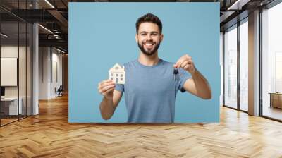 Young smiling man in casual clothes posing isolated on blue wall background, studio portrait. People sincere emotions lifestyle concept. Mock up copy space. Holding in hands house and bunch of keys. Wall mural