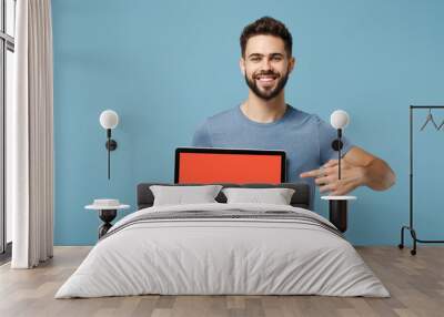 Young smiling man in casual clothes posing isolated on blue wall background in studio. People lifestyle concept. Mock up copy space. Point index finger on laptop pc computer with blank empty screen. Wall mural