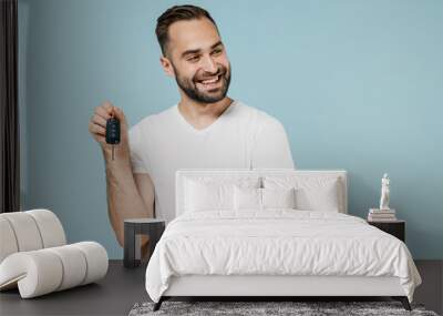 Young smiling minded happy man in blank print design white t-shirt hold in hand car key fob keyless system look aside on workspace area isolated on plain pastel light blue background studio portrait Wall mural