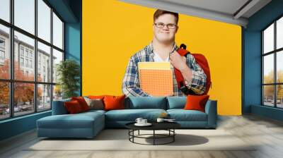 Young smiling smart man with down syndrome wear glasses casual clothes backpack look camera hold books go to school isolated on pastel plain yellow color background. Genetic disease world day concept. Wall mural