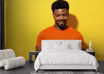 Young smiling student man of African American ethnicity 20s wear orange t-shirt read novel book learn prepare before exam isolated on plain yellow background studio portrait. People lifestyle concept. Wall mural