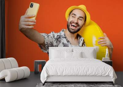 Young smiling tourist man wear beach shirt hat hold inflatable ring doing selfie shot on mobile cell phone isolated on plain orange background studio portrait Summer vacation sea rest sun tan concept Wall mural