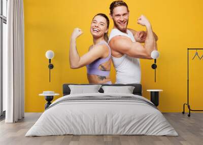 Young strong fitness trainer two man woman wearing blue clothes spend time in home gym showing biceps muscles on hand stand back to back isolated on plain yellow background. Workout sport fit concept. Wall mural