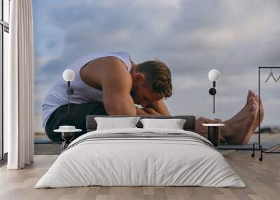 Young strong sporty fit sportsman man he wears sports clothes do stretch exercise for legs, sit at floor warm up train at sunrise sun dawn over sea beach outdoor on pier seaside in summer day morning. Wall mural