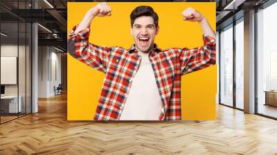 Young strong sporty fitness man he wears red checkered shirt casual clothes showing biceps muscles on hand demonstrating strength power isolated on plain yellow orange background. Lifestyle concept. Wall mural