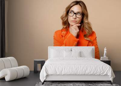 Young successful employee business woman corporate lawyer 30s wears classic formal orange suit glasses work in office prop up chin look aside on area isolated on plain beige color background studio. Wall mural